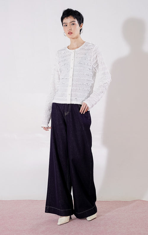 Outer crop wanita lengan panjang Anandra Top dari This Is April berwarna putih dengan detail tekstur renda horizontal berlapis dan material sheer menerawang, digantung di rak pakaian.