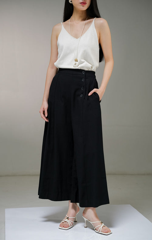 Celana panjang kulot wanita This Is April Blakeley Pants warna hitam pekat, model high-waist dengan detail tiga deret kancing hidup asimetris di bagian pinggang sisi kiri depan.
