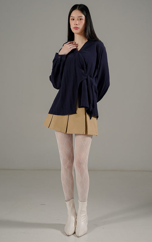 Bryanna Top Navy, atasan blus lengan panjang wanita warna biru dongker dengan kerah V dan detail tali pengikat di bagian tengah dan samping untuk merampingkan pinggang.