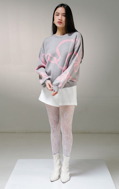 Atasan sweater rajut lengan panjang wanita This Is April Callie Sweater warna abu-abu (grey), model kerah bulat dengan detail motif grafis jalinan pita warna merah muda (pink) di bagian depan dan lengan.