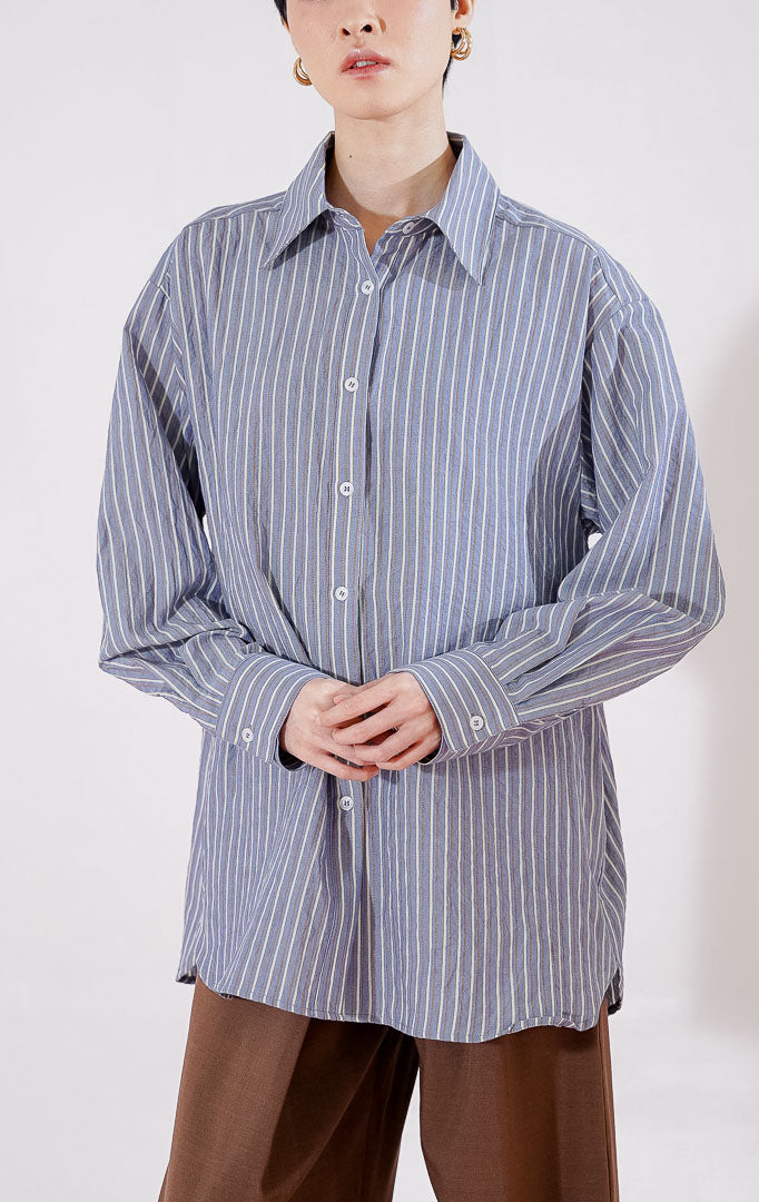 Kemeja wanita lengan panjang Carmela Top dari This Is April berwarna navy dengan motif garis vertikal putih tipis (pin stripes), bertekstur crinkle halus, dilengkapi kerah klasik dan kancing depan, digantung di rak pakaian.