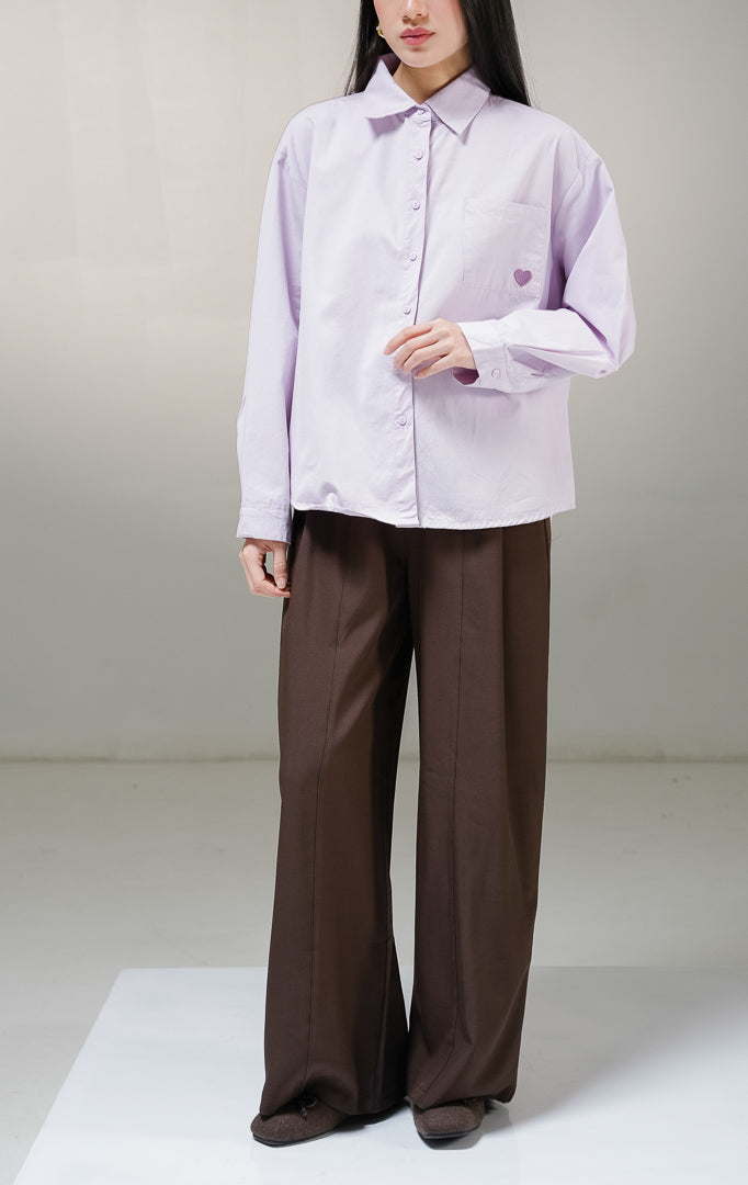 Kemeja basic lengan panjang wanita This Is April Claudette Top warna ungu muda (light purple), dilengkapi satu saku di dada kiri dengan detail bordiran bentuk hati kecil warna ungu tua.