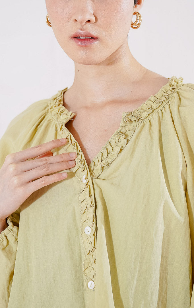 Blouse lengan panjang wanita This Is April Eloise Top warna khaki berbahan katun, dengan kerah V-neck beraksen ruffle, kancing depan, dan ujung lengan karet.