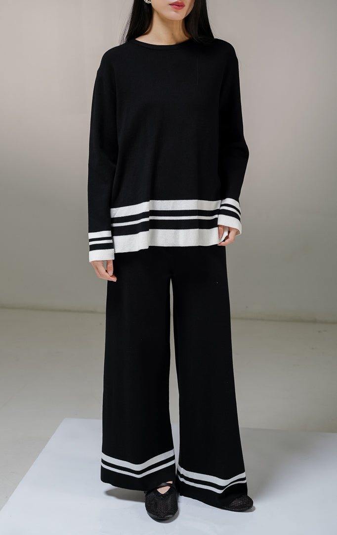 Setelan one set wanita This Is April Espera Set warna hitam, terdiri dari atasan sweater rajut lengan panjang kerah bulat dan celana panjang rajut dengan detail aksen garis horisontal warna putih di bagian ujung bawah.