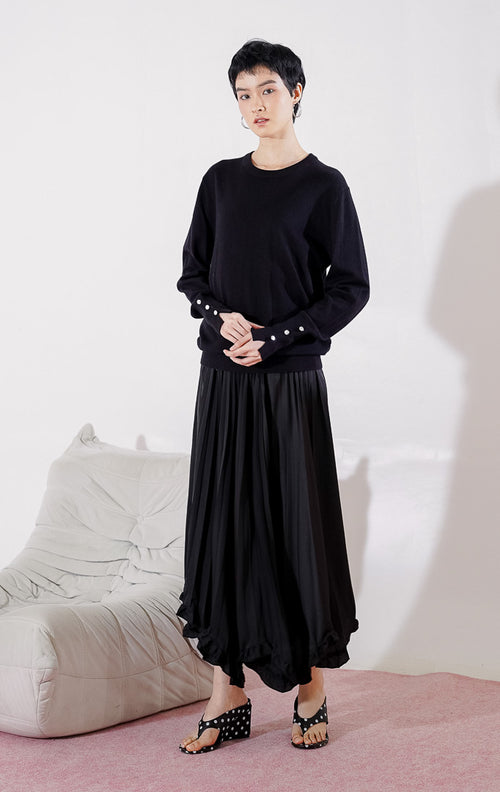 Sweater rajut wanita lengan panjang Gamora Sweater dari This Is April berwarna hitam pekat berdesain minimalis polos, kerah bulat (crewneck), dan dilengkapi aksen kancing perak elegan di bagian ujung lengan.