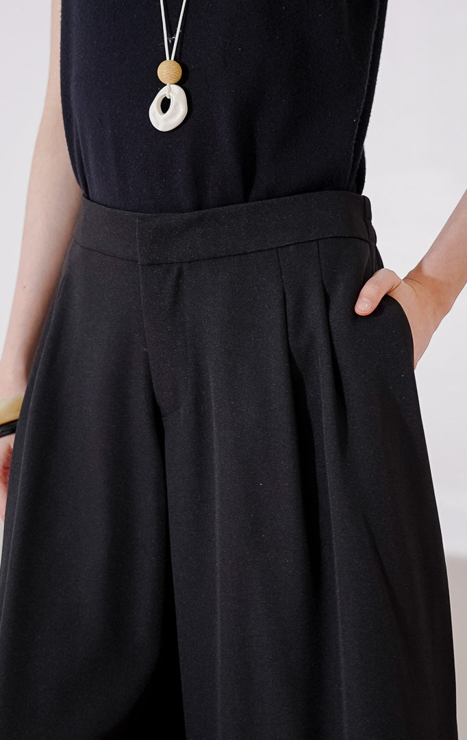 Celana bermuda wanita This Is April Hiraeth Pants warna hitam, berpotongan wide-leg yang longgar, dengan detail lipit rapi di bagian depan dan pinggang karet di bagian belakang.