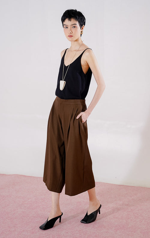 Celana panjang wanita This Is April Hiraeth Pants warna dark brown, berpotongan longgar dengan detail ritsleting depan, dua saku samping, dan karet pinggang di bagian belakang