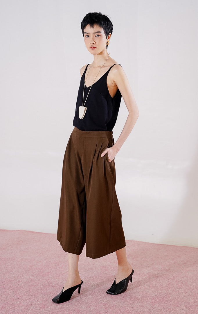 Celana panjang wanita This Is April Hiraeth Pants warna dark brown, berpotongan longgar dengan detail ritsleting depan, dua saku samping, dan karet pinggang di bagian belakang
