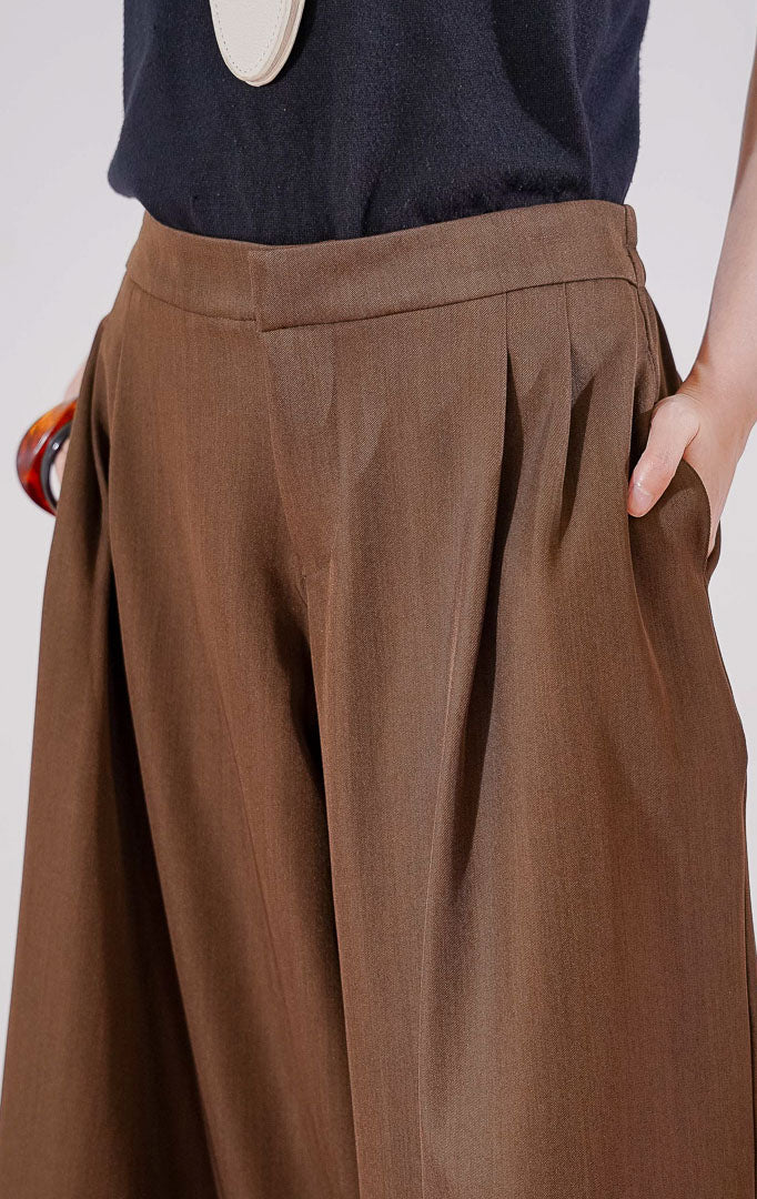 Celana panjang wanita This Is April Hiraeth Pants warna dark brown, berpotongan longgar dengan detail ritsleting depan, dua saku samping, dan karet pinggang di bagian belakang
