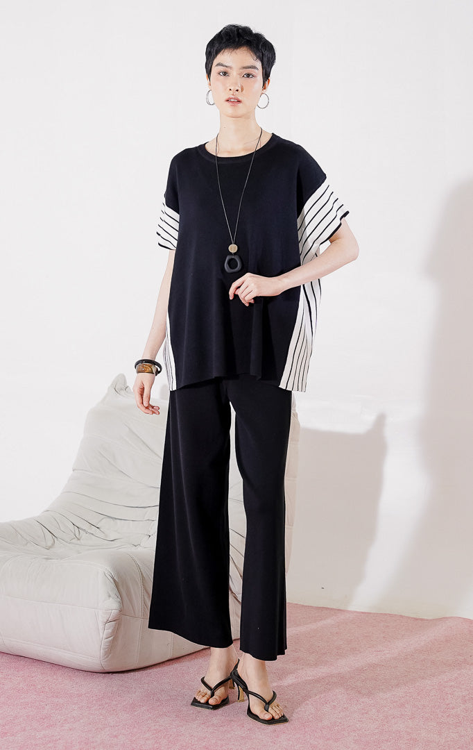 Baju setelan rajut wanita Kanza Set Black dari This Is April berwarna hitam dengan detail garis vertikal putih di bagian lengan, digantung di rak pakaian.