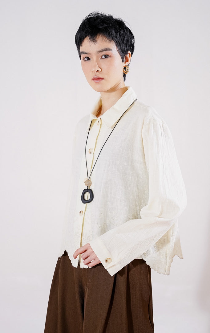 Kemeja lengan panjang wanita This Is April Layne Top warna ivory berbahan katun linen, berkerah klasik, dengan kancing depan dan detail bordir floral pada ujung bawah bergelombang