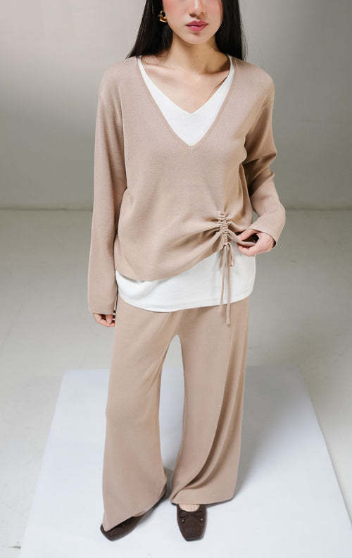 Setelan one set wanita This Is April Millicent Set warna khaki (cokelat muda), terdiri dari atasan sweater rajut lengan panjang kerah v-neck dengan aksen layer putih di leher dan ujung bawah baju, serta celana panjang rajut senada.