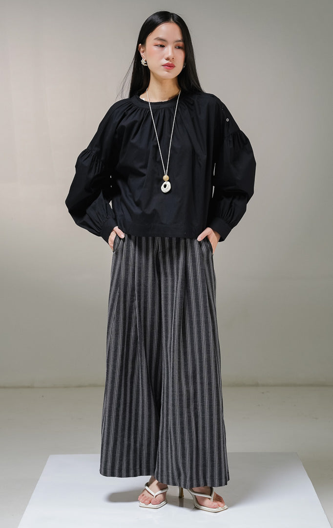 Blouse lengan panjang wanita This Is April Morgana Top warna hitam, model crewneck dengan detail kerutan penuh di sekeliling leher dan deretan kancing aktif di sisi bahu kiri.