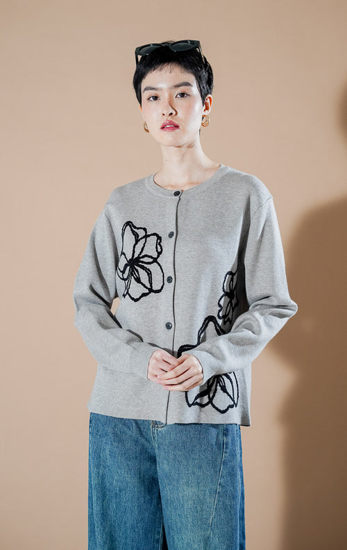 Peppie Cardigan Grey dari This Is April, cardigan rajut warna abu-abu dengan detail bordir bunga hitam di sisi depan dan kancing aktif.