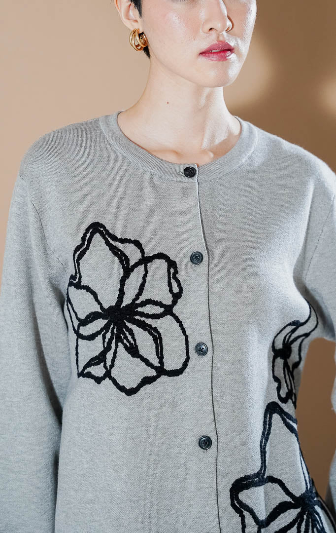Peppie Cardigan Grey dari This Is April, cardigan rajut warna abu-abu dengan detail bordir bunga hitam di sisi depan dan kancing aktif.