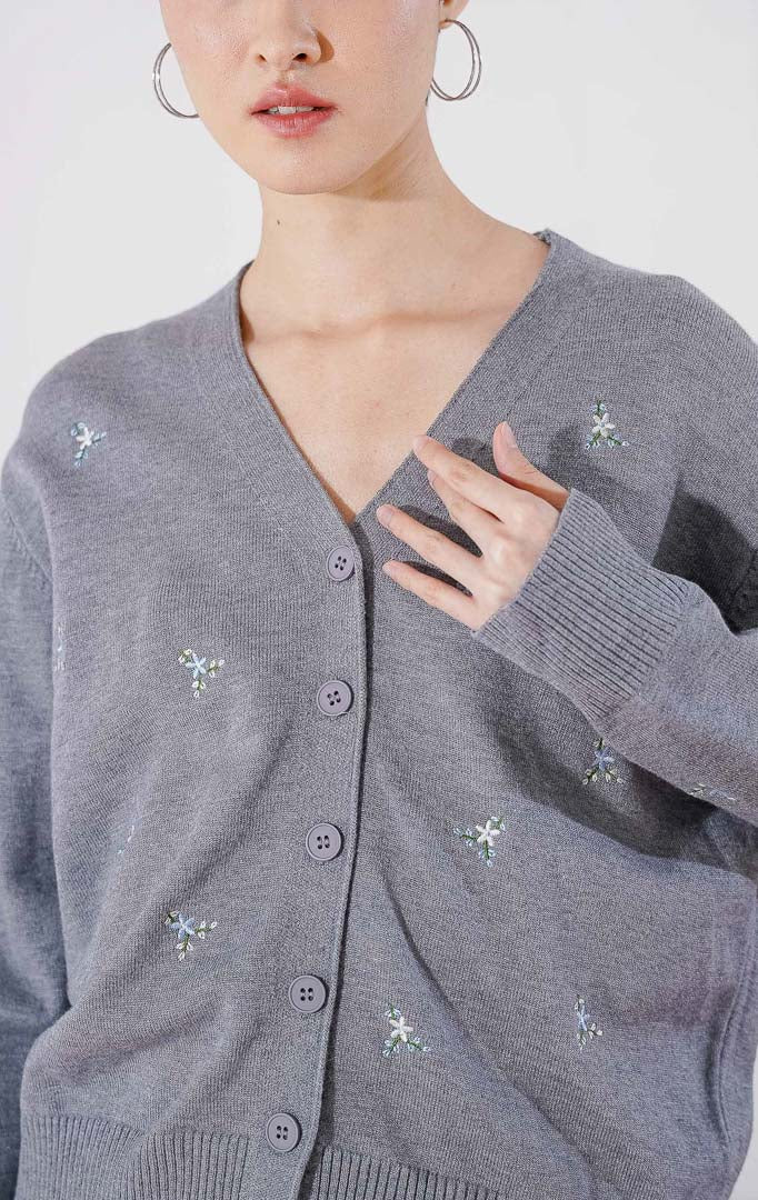 Tampak depan This Is April Petunia Cardigan warna abu-abu, berupa cardigan rajut lengan panjang kerah V-neck dengan kancing depan dan detail motif bordir bunga kecil yang tersebar.