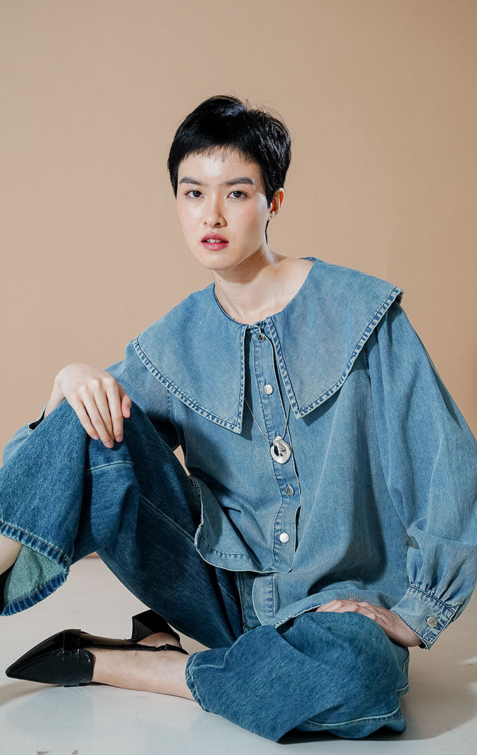 Poppi Top Denim dari This Is April, kemeja denim lengan panjang warna biru dengan detail kerah pelaut (sailor collar) yang lebar dan kancing depan perak.