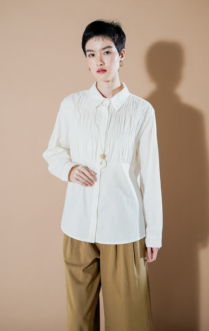 Valuna Top White dari This Is April, kemeja katun lengan panjang warna putih dengan detail kerutan (smocked texture) pada bagian dada dan kancing depan.