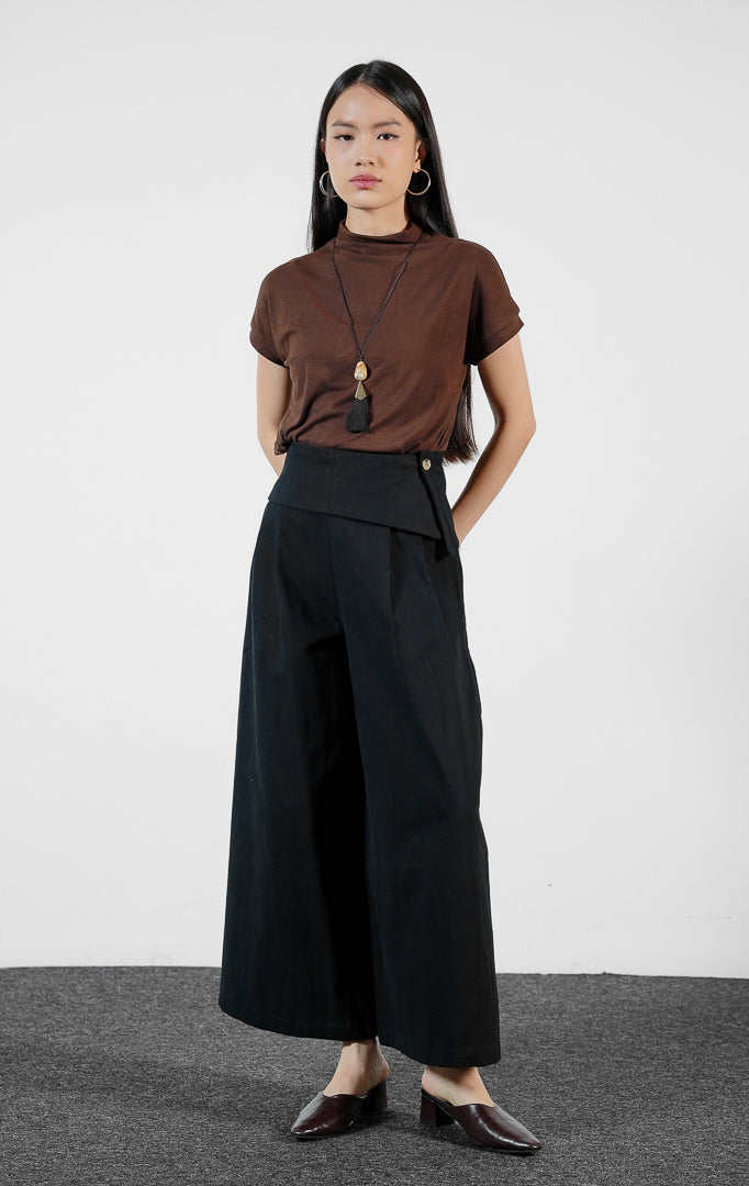 Bawahan wanita model celana panjang katun potongan lebar (black wide-leg pants) Christa Pants dengan detail pinggang lipat (fold-over waistband) warna hitam yang struktural dan elegan.