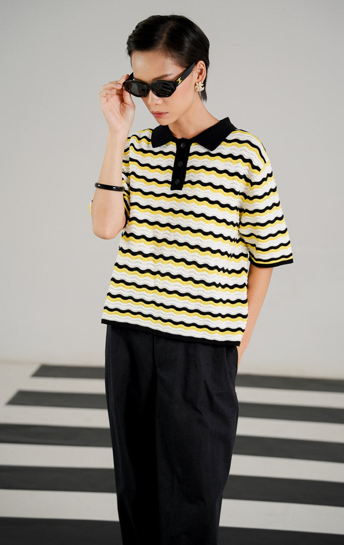 Atasan rajut wanita lengan pendek bermotif garis gelombang (wavy) perpaduan warna kuning, putih, dan hitam, dilengkapi kerah polo hitam dan kancing depan dari This Is April.