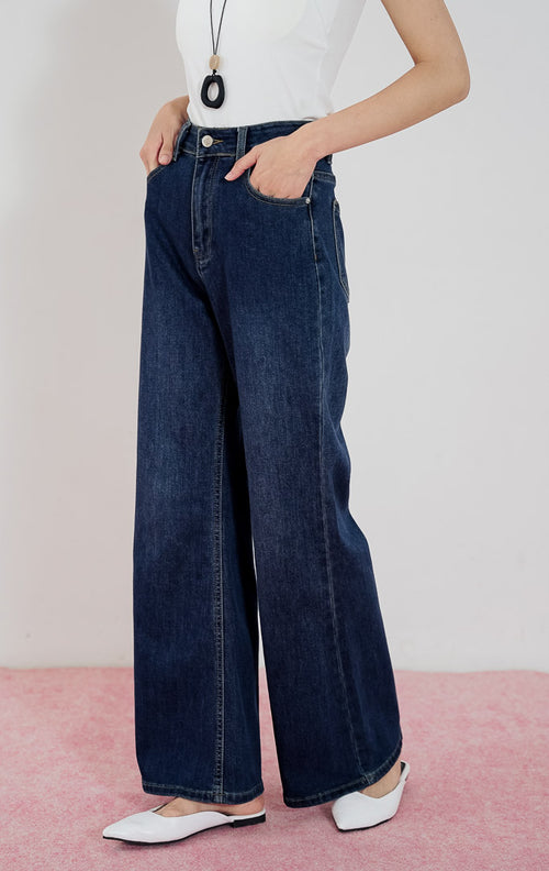 Model mengenakan celana jeans wanita This Is April Dolores warna dark denim berpotongan wide-leg, dipadukan dengan tanktop putih dan kalung aksesoris.