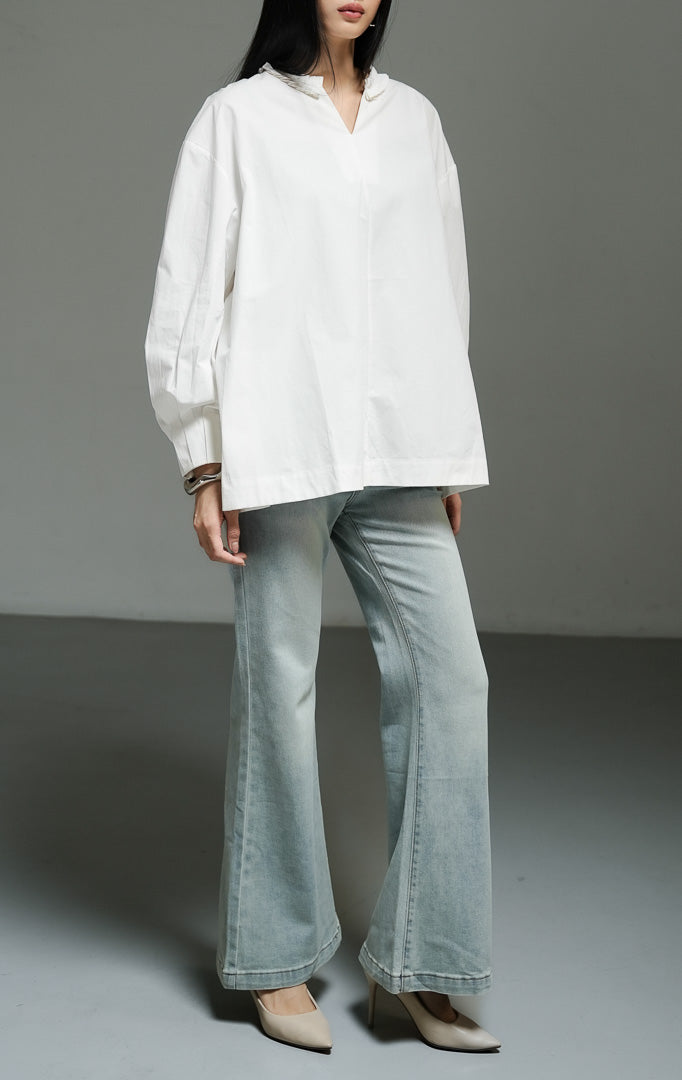 Blus wanita lengan panjang warna putih (white pleated-trim stand collar blouse) Florina Top dengan bahan katun poplin klasik berstruktur, kerah tegak beraksen trim plisket, serta siluet longgar yang bersih.