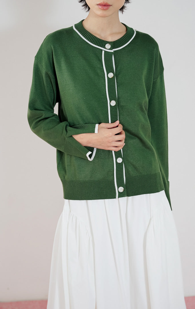 Model mengenakan This Is April Forest Cardigan warna dark green, kardigan rajut lengan panjang dengan detail garis putih kontras (contrast tipping) dan kancing depan.