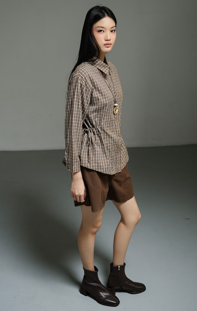 Kemeja wanita lengan panjang motif kotak-kotak warna cokelat (brown plaid drawstring shirt top) Hilaria Top dengan bahan katun non-stretch berkualitas, penutup kancing depan, serta tali serut pinggang untuk siluet yang ramping dan rapi.