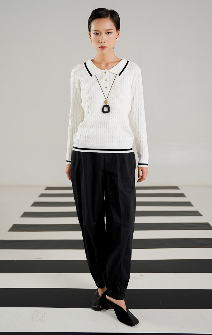 Sweater rajut kabel (cable knit) wanita lengan panjang warna putih dengan kerah polo, detail tiga kancing emas di dada, serta aksen garis hitam di kerah dan ujung baju dari This Is April.
