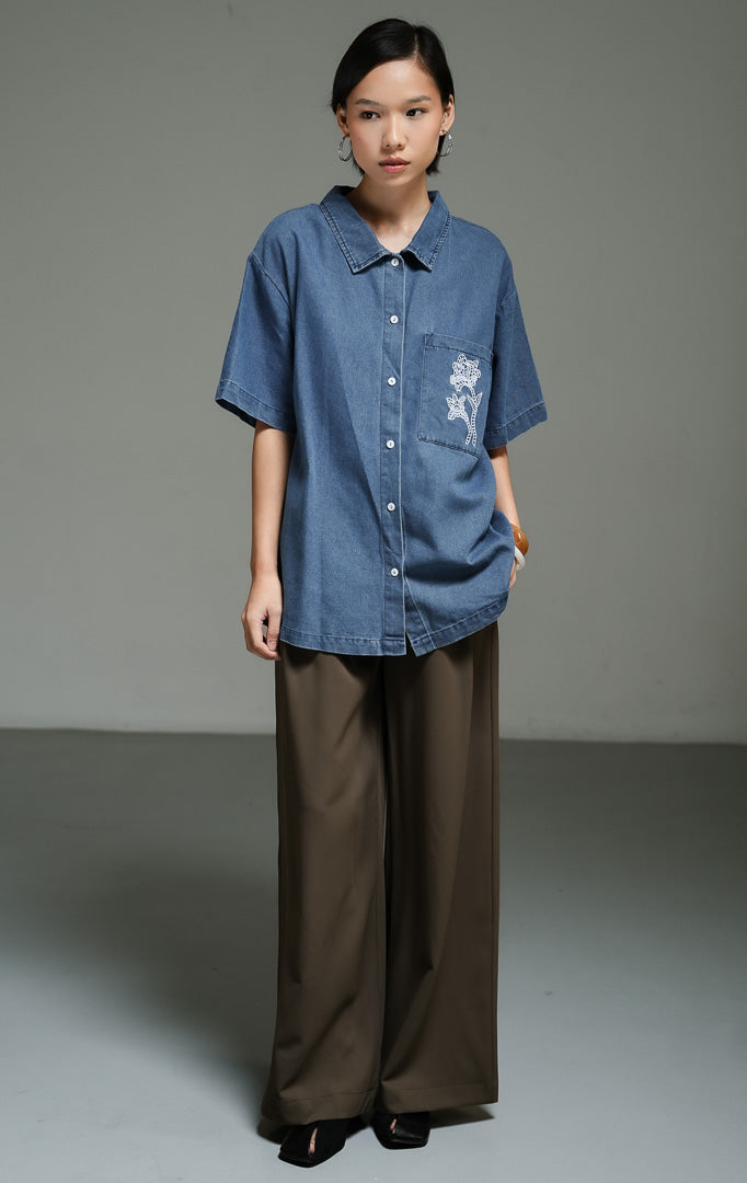 Atasan wanita model kemeja denim lengan pendek warna dark denim dengan detail bordir renda bunga pada bagian saku (dark denim floral lace embroidery shirt top) Kaelina Top yang gaya dan kasual.