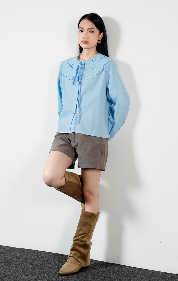 Pakaian wanita model blouse lengan panjang bahan katun dengan detail kerah bordir motif lubang (eyelet broderie) dan tepi gelombang (scalloped edges) warna biru muda Lioren Top untuk gaya kasual anggun.