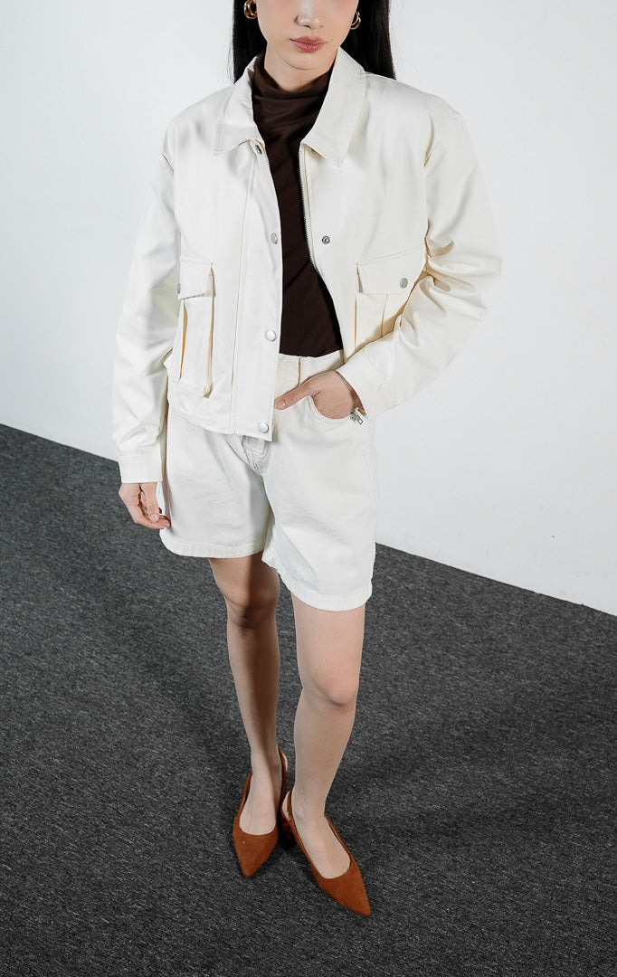 Pakaian wanita model jaket lengan panjang bahan katun warna ivory dengan detail saku penutup dan lipatan lipit (ivory box-pleated flap pocket jacket) Lisande Jacket untuk gaya kasual yang rapi.