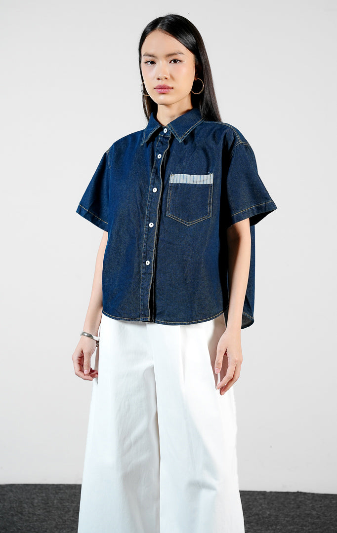 Pakaian wanita model kemeja denim pendek warna biru tua dengan detail saku dada beraksen garis (stripe-trimmed chest pocket shirt) Luniel Top untuk gaya kasual modern yang stylish.