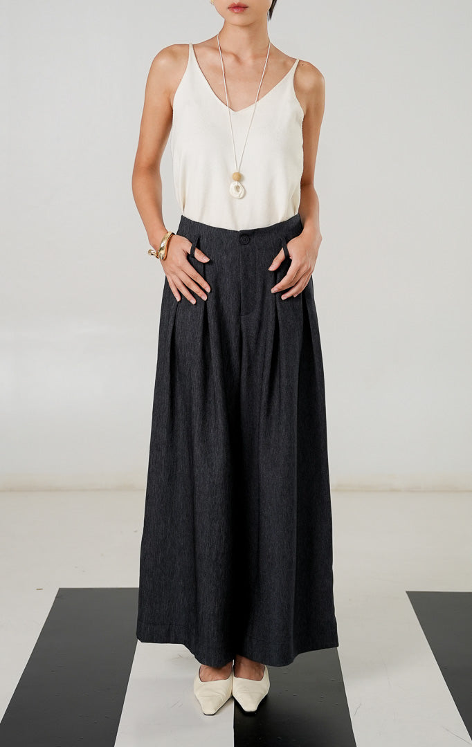 Celana panjang wanita berpotongan lebar (wide leg) warna abu abu tua (dark grey) dengan detail kancing depan, resleting, lipatan (pleats), dan pinggang karet dari This Is April.