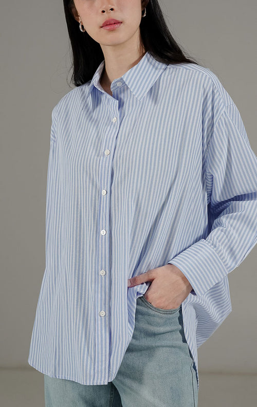 Olivier Top Light Blue dari This Is April, kemeja oversize motif salur vertikal biru putih dengan potongan asimetris dan kancing depan.