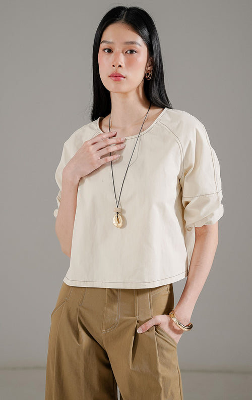 Quincy Top Ivory dari This Is April, atasan lengan panjang wanita warna putih gading dengan detail jahitan cokelat kontras di seluruh siluet dan pergelangan tangan karet.