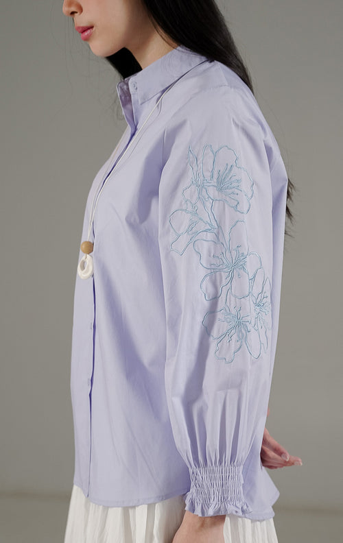 Vayla Top Blue dari This Is April, kemeja biru muda wanita dengan bordir bunga di bagian lengan dan detail pergelangan tangan karet.