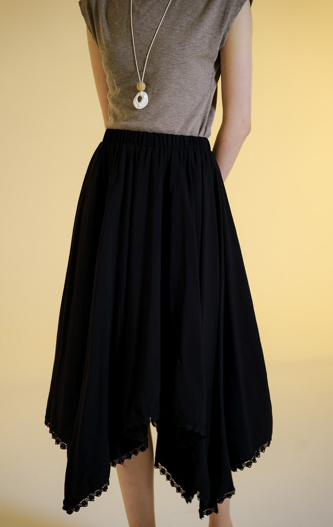 Pakaian wanita model rok panjang maxi dengan pinggang karet dan potongan bawah asimetris dilapisi renda (uneven lace trim flowy maxi skirt) warna hitam Villera Skirt untuk gaya kantor dan kasual anggun.