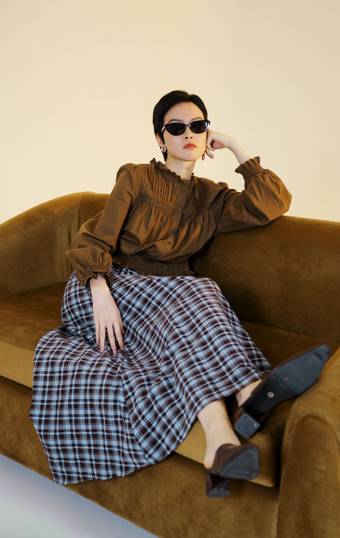 Pakaian wanita model blouse katun lengan panjang dengan detail lipit pada bagian dada dan potongan peplum (pin-tucked peplum blouse) warna cokelat tua Violetta Top untuk gaya kasual anggun.
