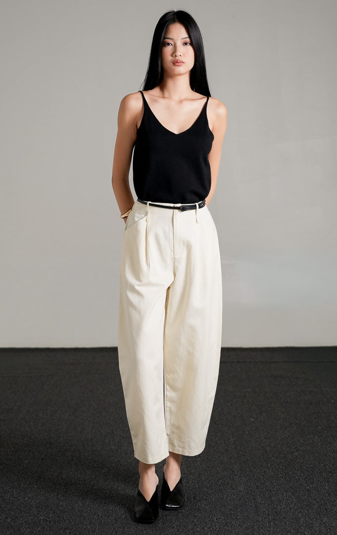 Timmy Pants Ivory, celana katun panjang warna putih gading dengan potongan barrel-leg yang melengkung unik, dipadukan dengan tank top hitam.