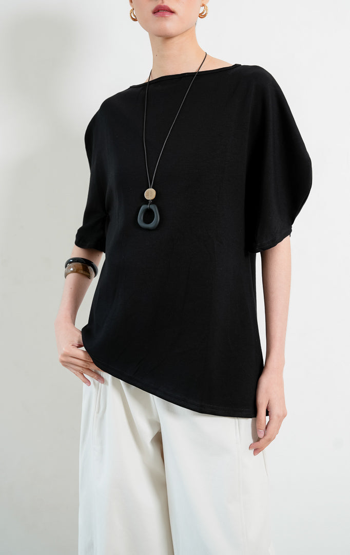 Blus wanita santai bahan campuran katun spandeks warna hitam (black cotton-spandex blouse) Tristian Top dengan kerah bulat klasik, siluet longgar (relaxed silhouette), dan detail lengan pendek melengkung unik (uniquely curved short sleeves).
