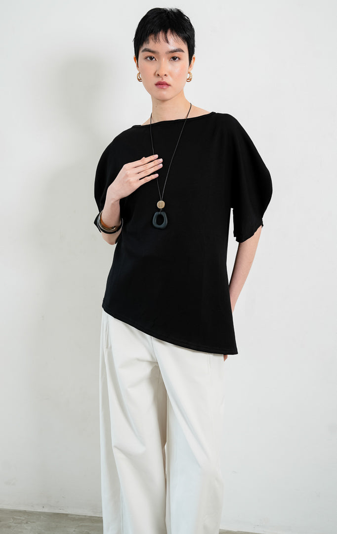 Blus wanita santai bahan campuran katun spandeks warna hitam (black cotton-spandex blouse) Tristian Top dengan kerah bulat klasik, siluet longgar (relaxed silhouette), dan detail lengan pendek melengkung unik (uniquely curved short sleeves).