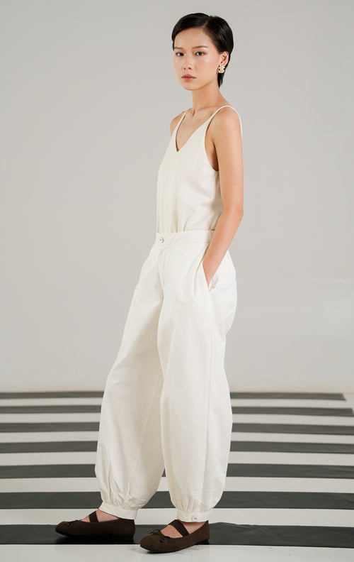 Celana panjang katun wanita Veilon Pants warna putih (White) dengan detail kancing di ujung kaki, lipit depan (pleats), dan ban pinggang karet belakang yang nyaman dari This Is April.