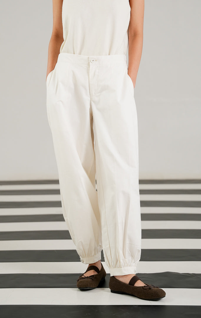 Celana panjang katun wanita Veilon Pants warna putih (White) dengan detail kancing di ujung kaki, lipit depan (pleats), dan ban pinggang karet belakang yang nyaman dari This Is April.