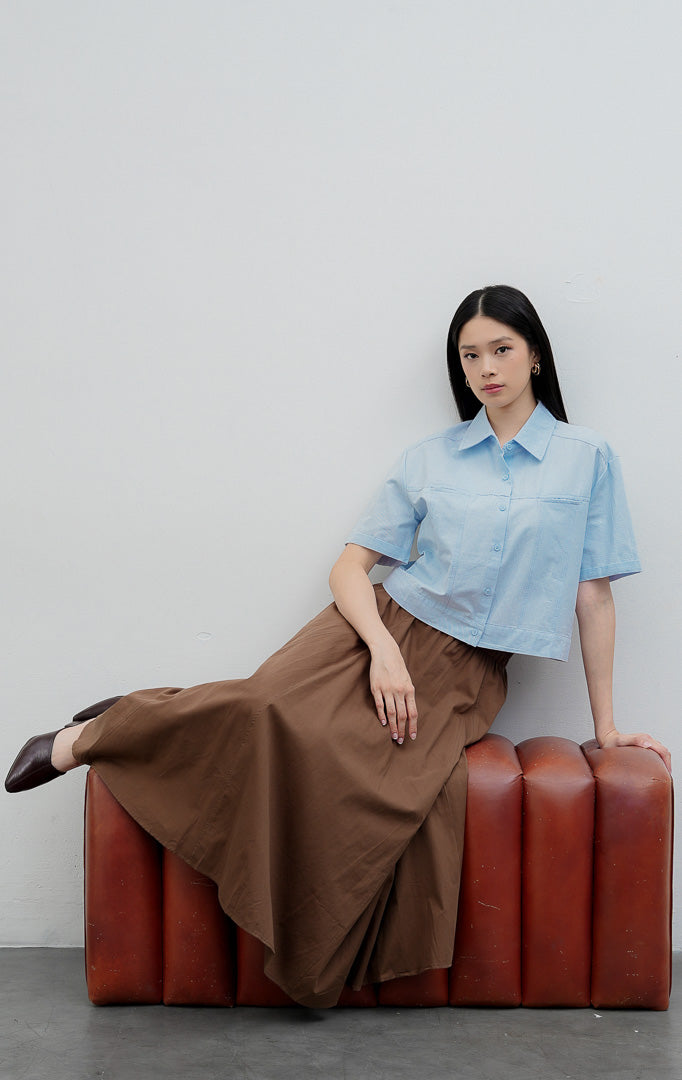 Kemeja kancing depan wanita warna biru muda (light blue) Velira Top berbahan katun terstruktur (structured cotton) dengan detail jahitan bahu (yoke seam detailing) dan lengan pendek.