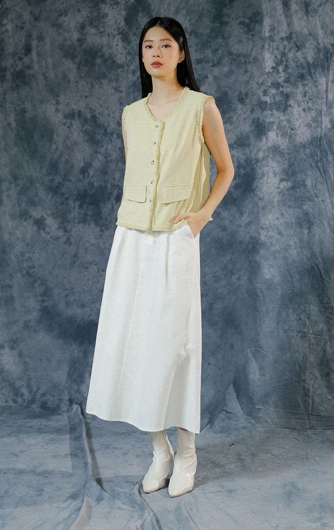 Atasan rompi wanita Venetia warna hijau muda (light green) tanpa lengan seperti pada foto menampilkan detail kancing depan, saku dengan penutup flap, dan aksen fringe/ruffle halus di sepanjang keliman.