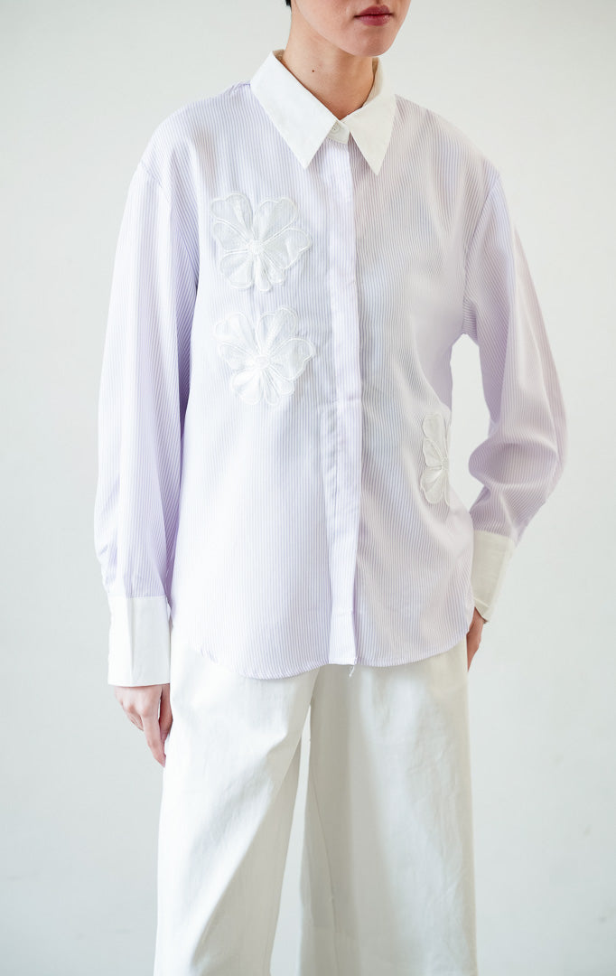 Kemeja wanita lengan panjang motif garis-garis ungu (purple vertical stripes) Wilfred Top dengan detail aplikasi bordir bunga (embroidered floral motifs), kerah dan manset kontras putih (contrasting pointed collar and cuffs), serta bukaan kancing depan.