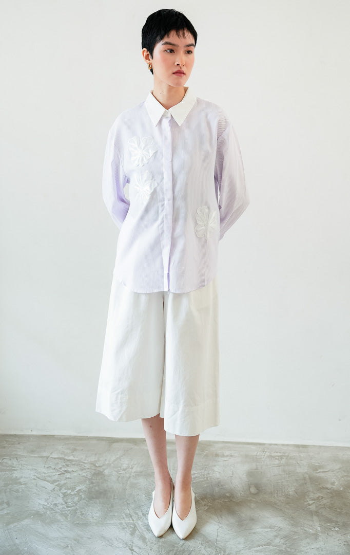 Kemeja wanita lengan panjang motif garis-garis ungu (purple vertical stripes) Wilfred Top dengan detail aplikasi bordir bunga (embroidered floral motifs), kerah dan manset kontras putih (contrasting pointed collar and cuffs), serta bukaan kancing depan.