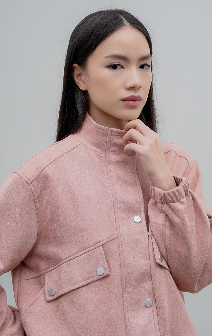 Jaket wanita berbahan suede warna merah muda pudar (dusty pink) Woolridge Jacket dengan kerah tinggi (high neck), saku dada fungsional, dan bukaan kancing jepret (snap buttons).