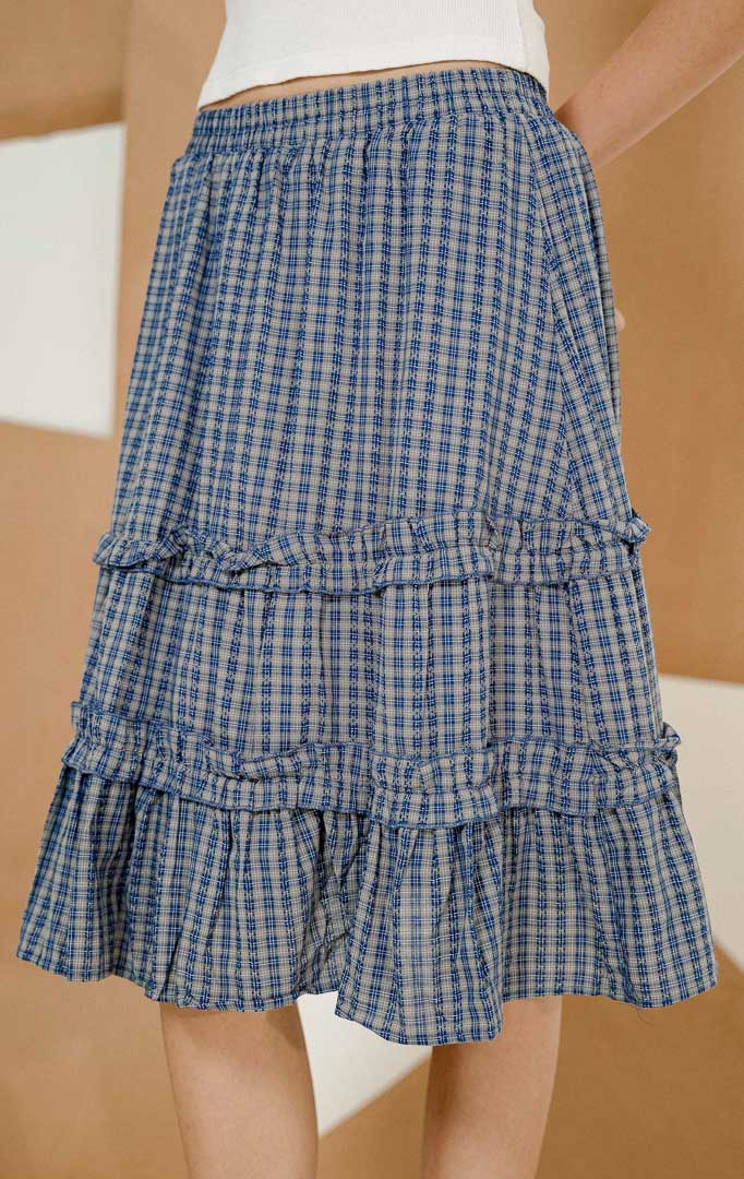 Model berpose mengenakan Yusion Plaid Tier Midi Skirt Navy, produk rok midi wanita motif kotak-kotak dengan model bertingkat dan pinggang karet elastis.